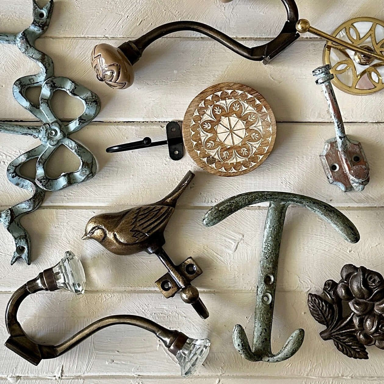 Assorted decorative hooks and vintage wall hardware lay on a pale wooden surface.