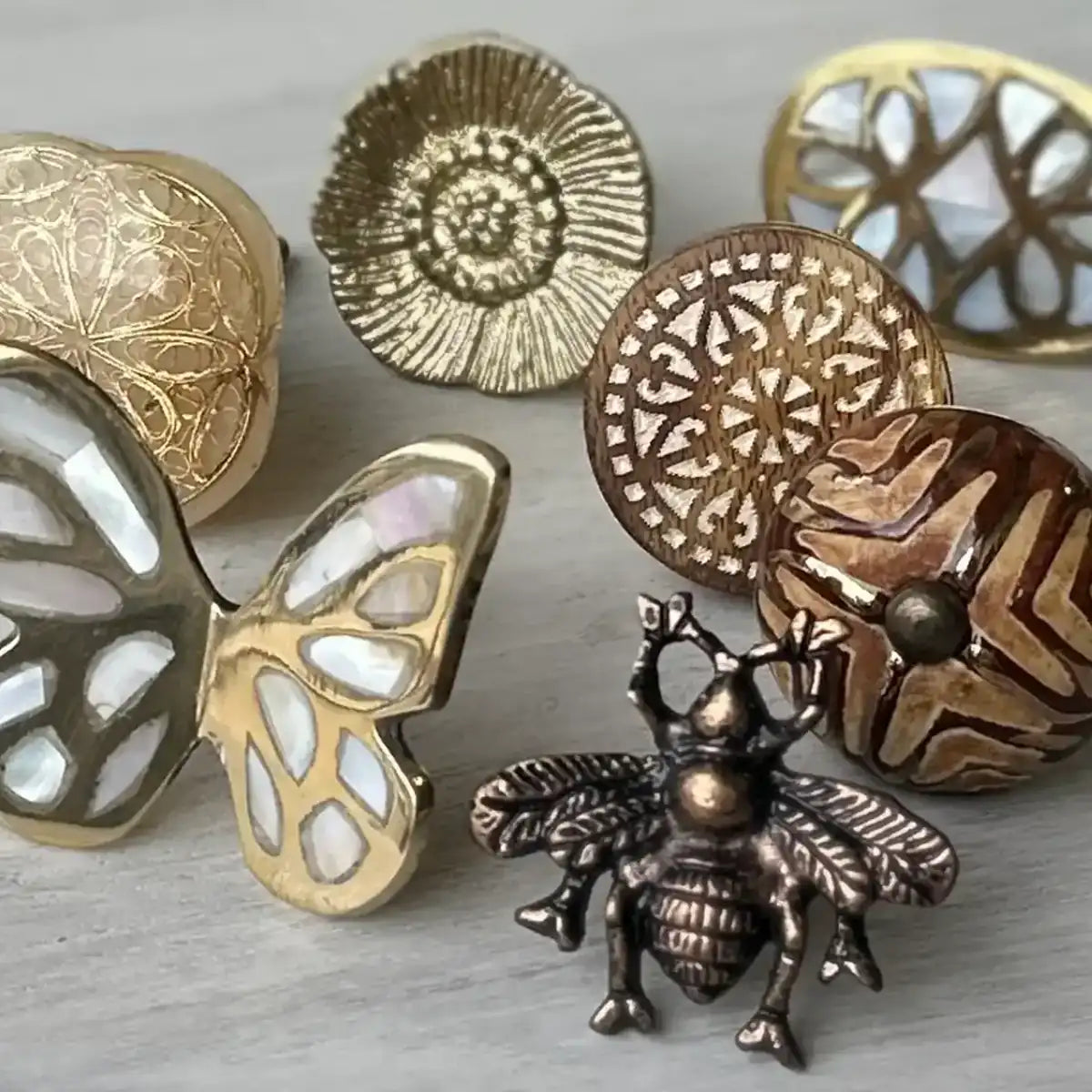 Decorative cabinetry handles, knobs, and pulls in metal finishes featuring floral, butterfly, and bee designs.