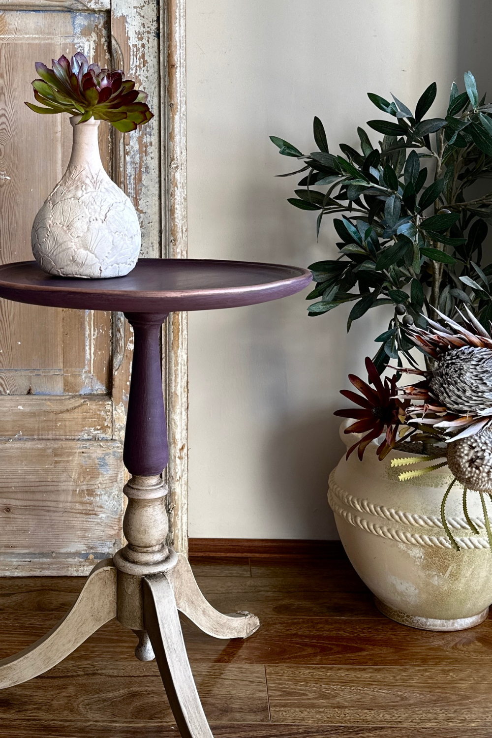 Small round table with a textured white vase and green plant against a wooden wall.