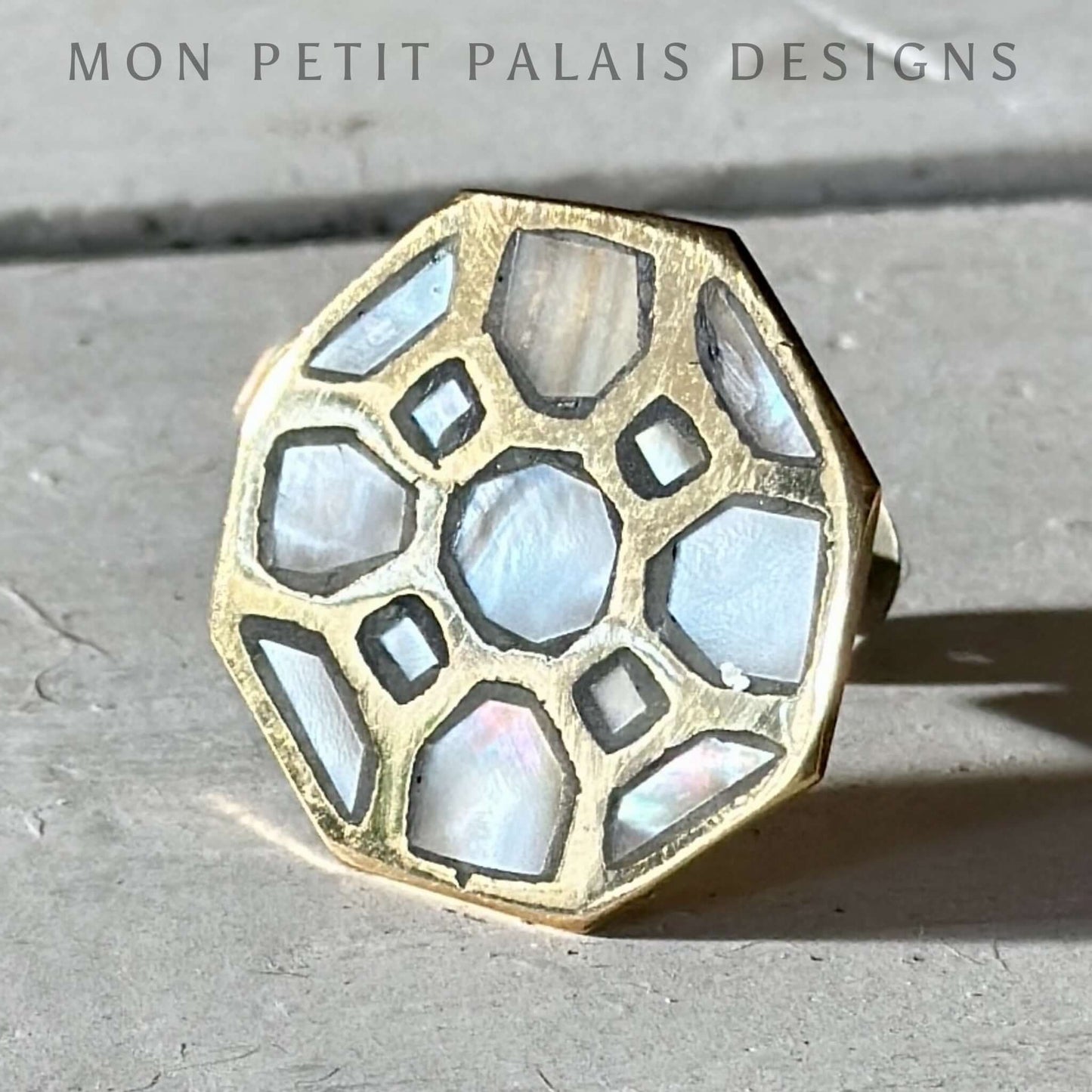 A gold hexagonal knob with mother of pearl inlay on a concrete background.