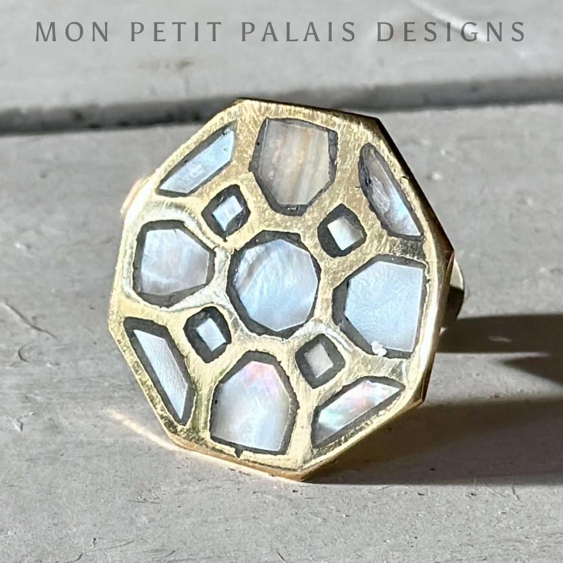 A gold hexagonal knob with mother of pearl inlay on a concrete background.