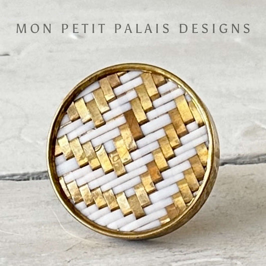 A round woven cabinet knob with a gold metal frame and white weaving, branded by MON PETIT PALAIS DESIGNS.