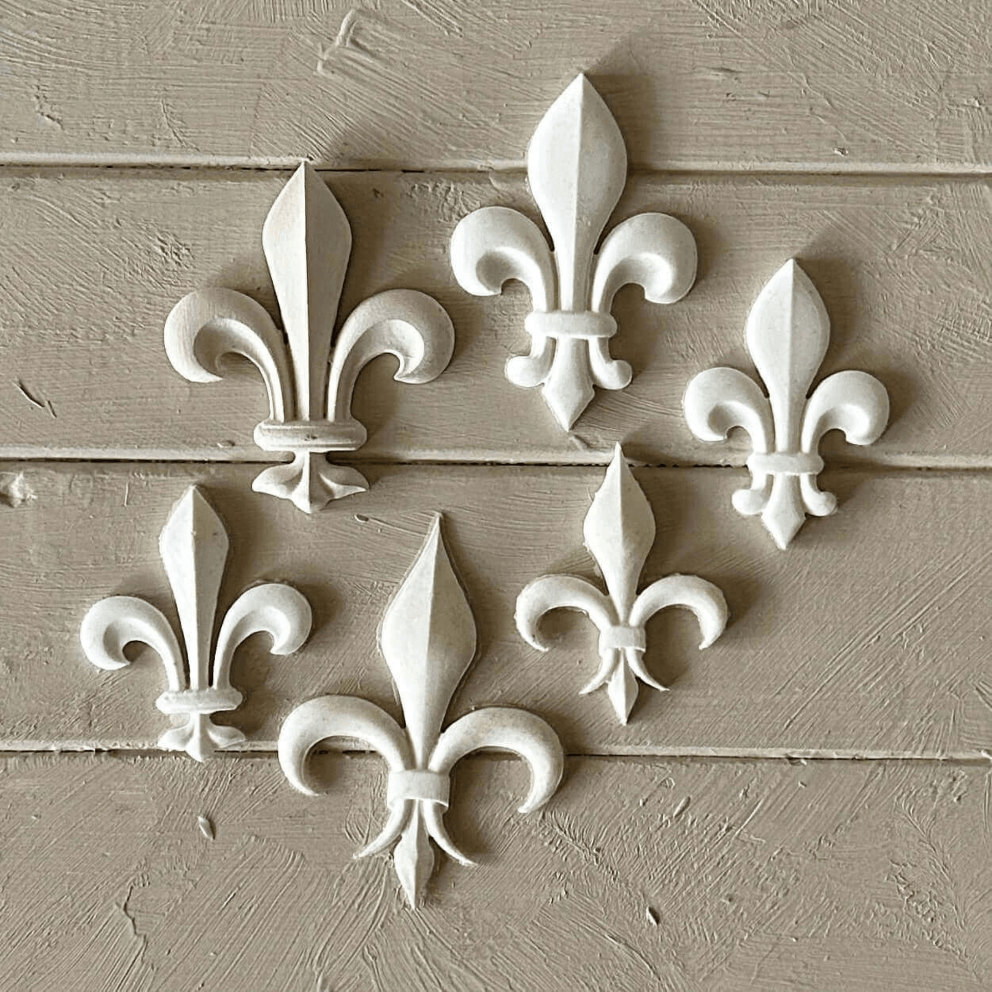 Fleur De Lis 002 - Resin Applique for Furniture & Crafts displayed in six elegant white designs on a wooden surface.
