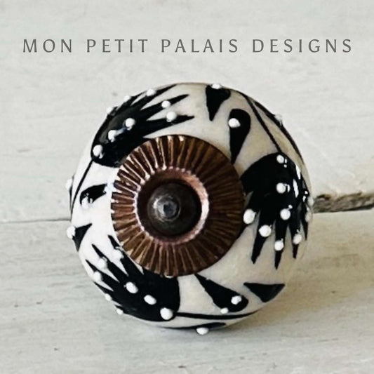 A black and cream ceramic knob with a geometric pattern and a bronze-toned central screw.