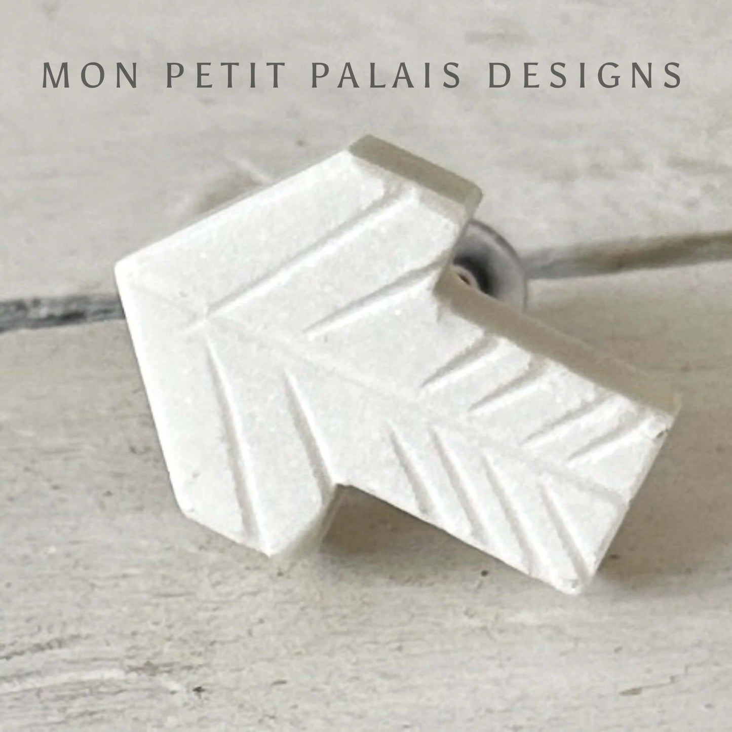 A white marble cabinet knob with an arrow design.