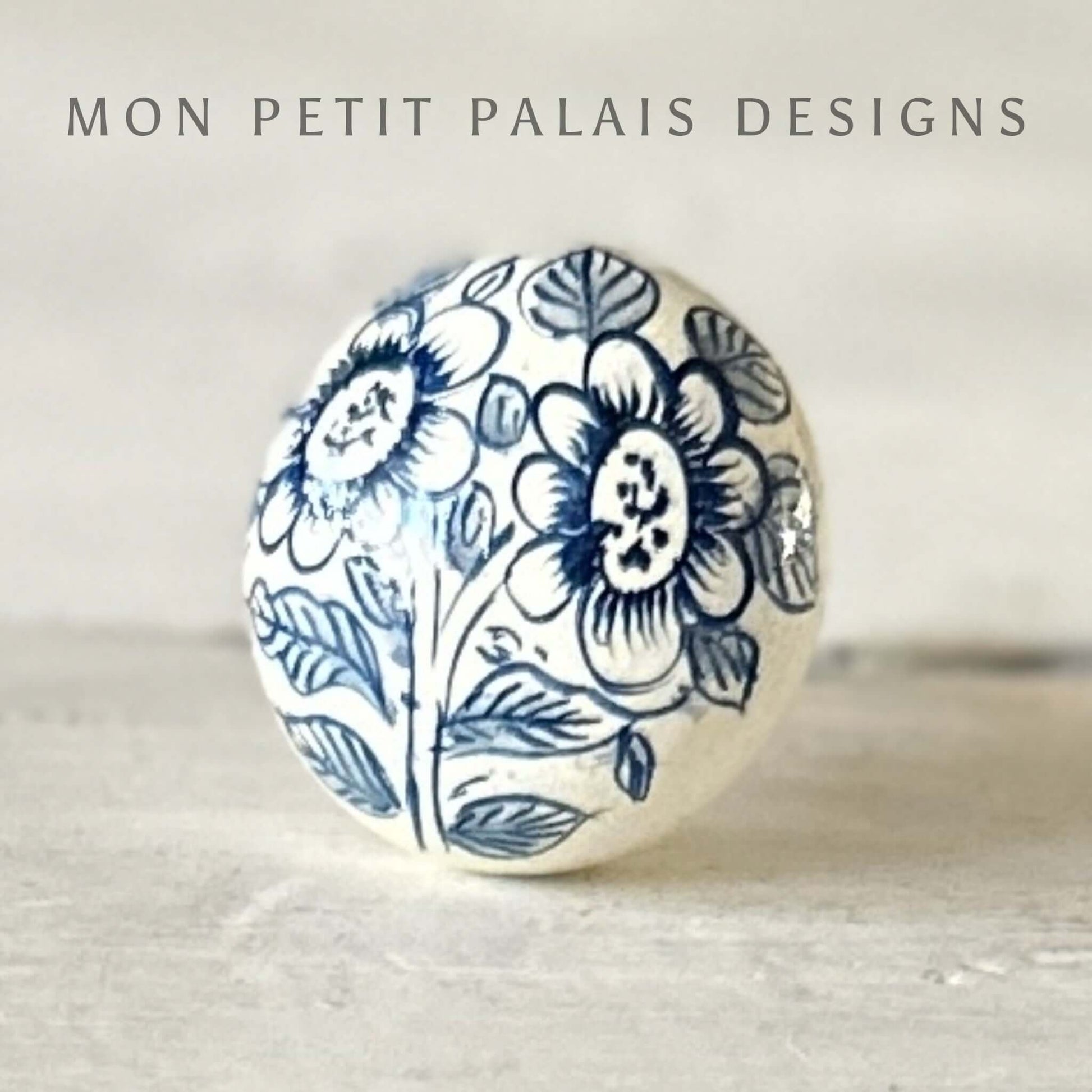 A round wooden painted knob with a blue and white floral pattern on a light background, with the text 'MON PETIT PALAIS DESIGNS' above it.