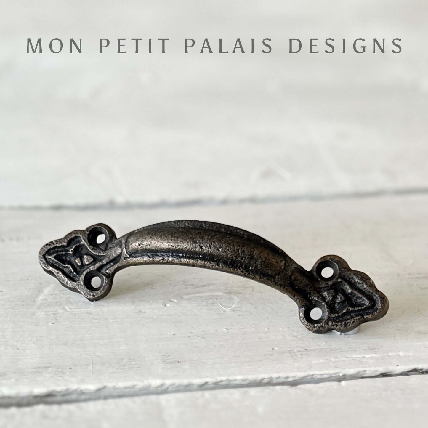 A  metal bar handle with a brass finish, displayed against a white wooden background.
