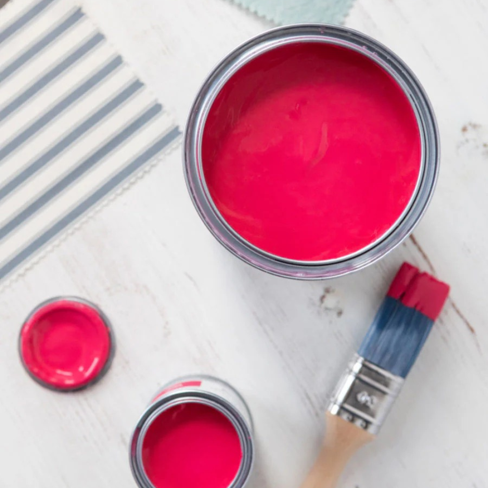 Flay lay of Annie Sloan Chalk Paint in Carpi Pink, featuring open paint tins and a brush on a white wood surface, styled with a striped fabric swatch