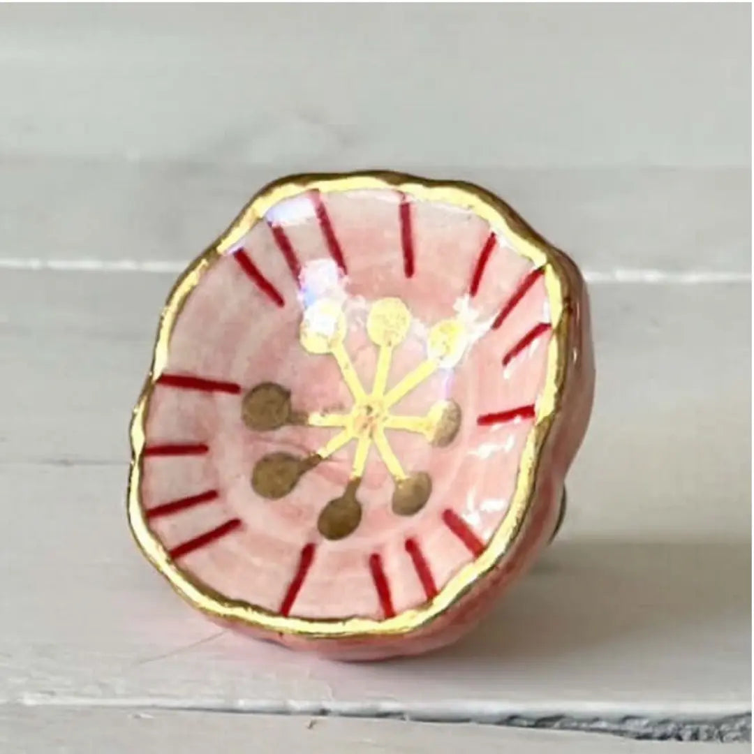 Blush and gold bloom ceramic knob close-up with red detail and gold edges.