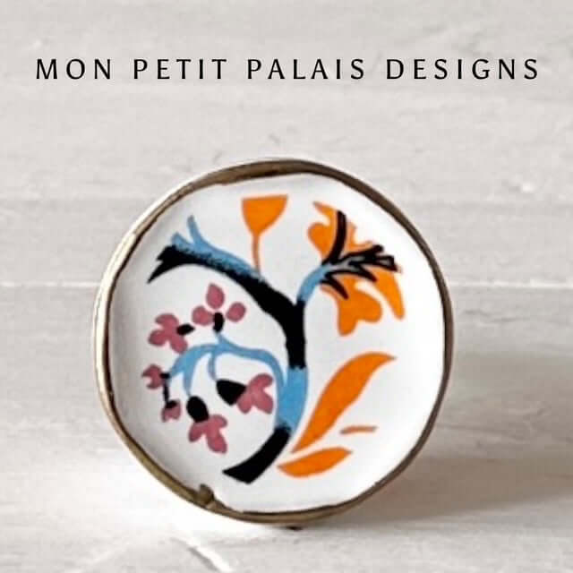 Orange & Blue Floral Hand-Painted Ceramic Knob with a bold boho floral design in blue, orange, and pink on a white ceramic base with gold trim.