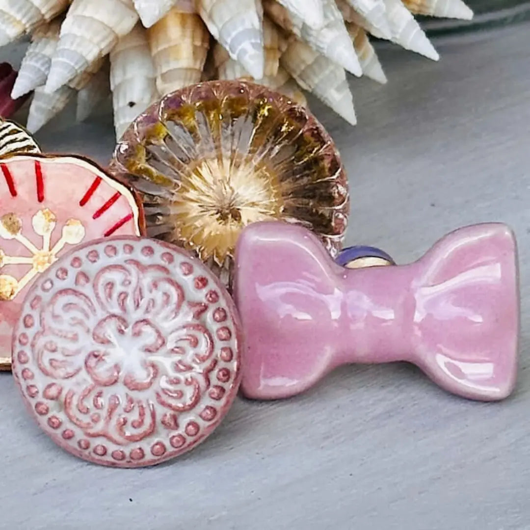 Pink Cute Ceramic Bow Cabinet Knob among decorative ceramic pieces on a rustic background.