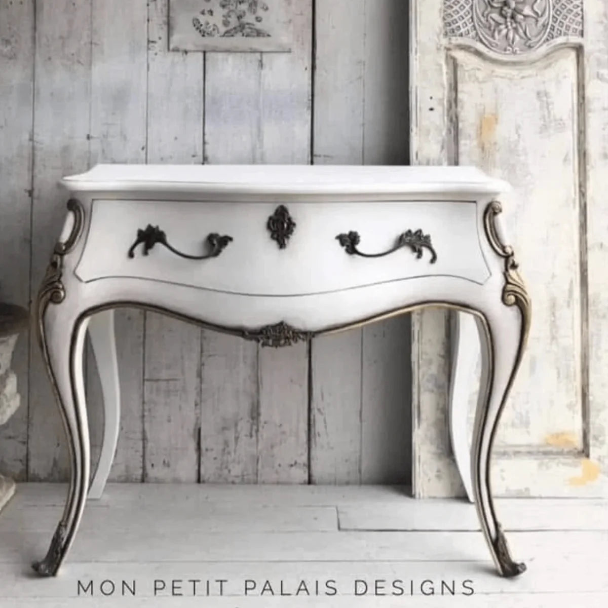 White console table with decorative legs against a wooden wall, featuring 'Mon Petit Palais Designs' branding.