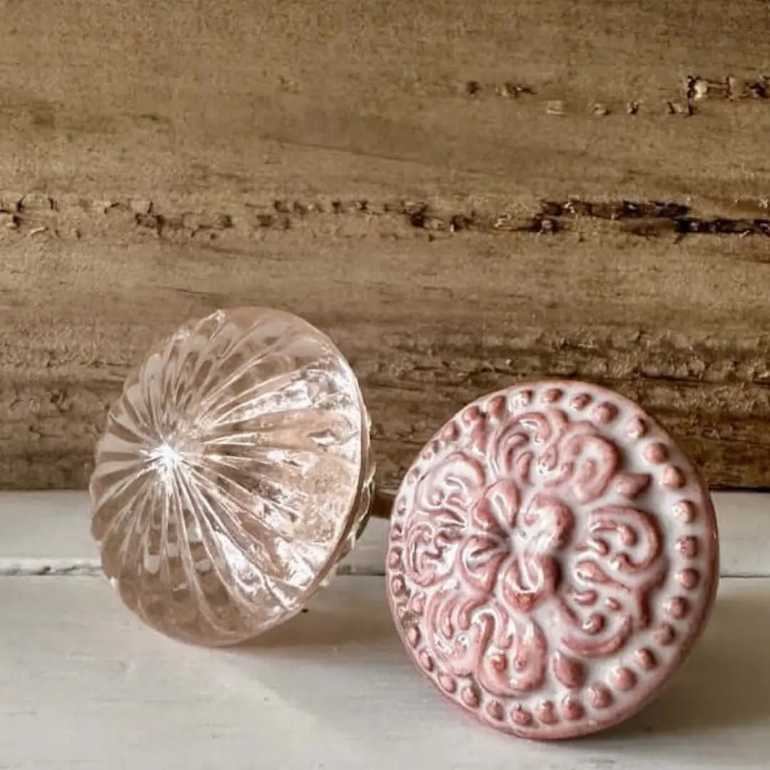 Rose Quartz Pink Glass Knob and Henrietta Rose Ceramic Knob displayed side by side. A vintage-inspired pink ceramic knob with an embossed floral design next to a faceted glass knob with a soft rose tint, perfect for upcycled furniture and cabinetry.