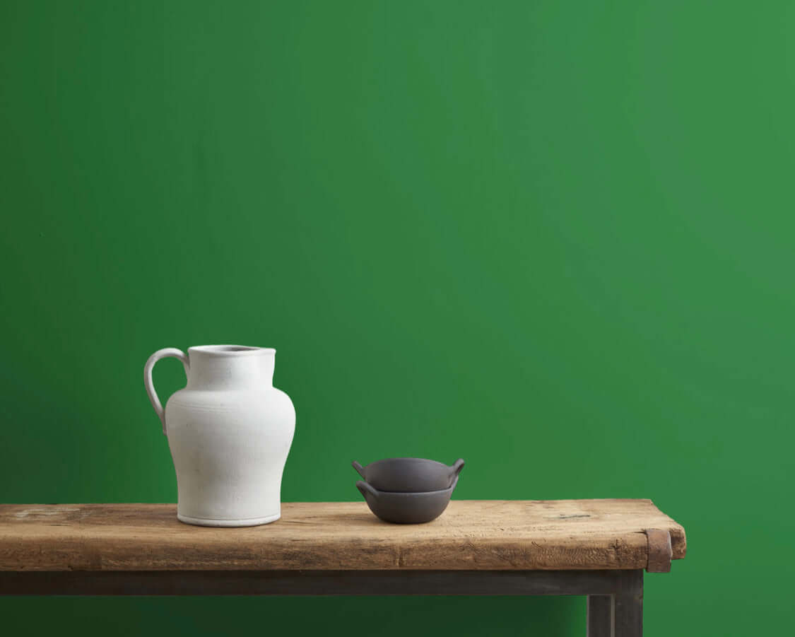 Schinkel Green Annie Sloan wall paint backdrop with a white pitcher and dark bowl on a rustic wooden table.