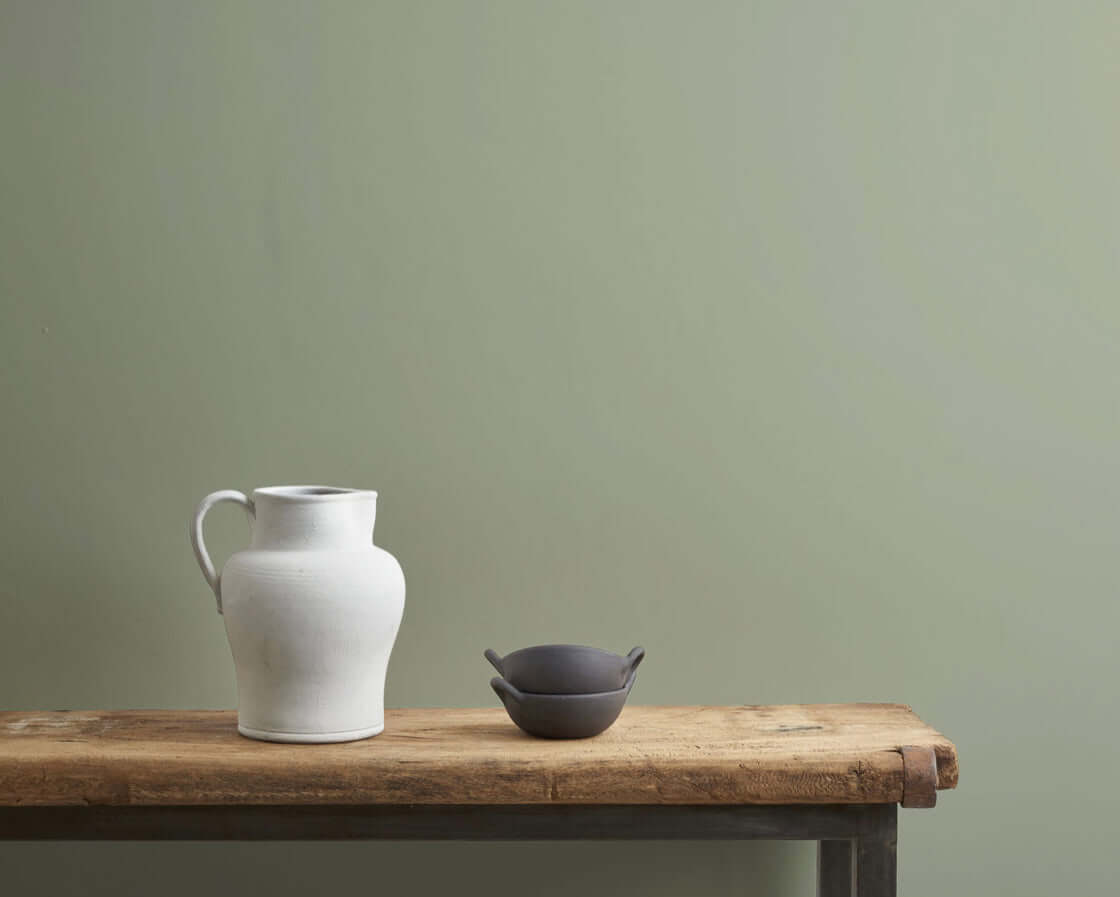 Two ceramic pieces on a wooden table in a room painted with Terre Verte by Annie Sloan.