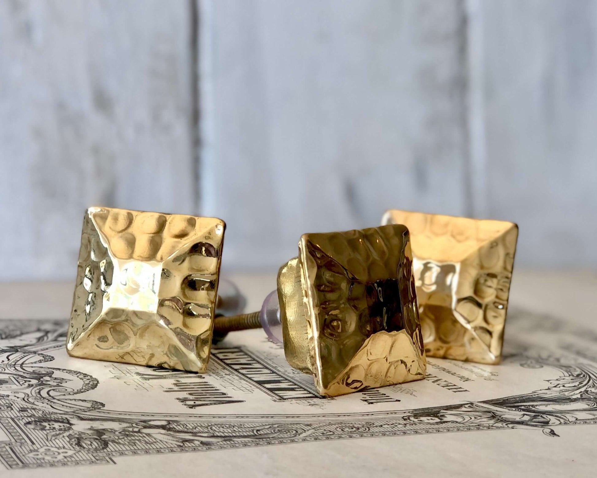 Group of Square Gold Cabinet Knobs styled together on rustic surface.