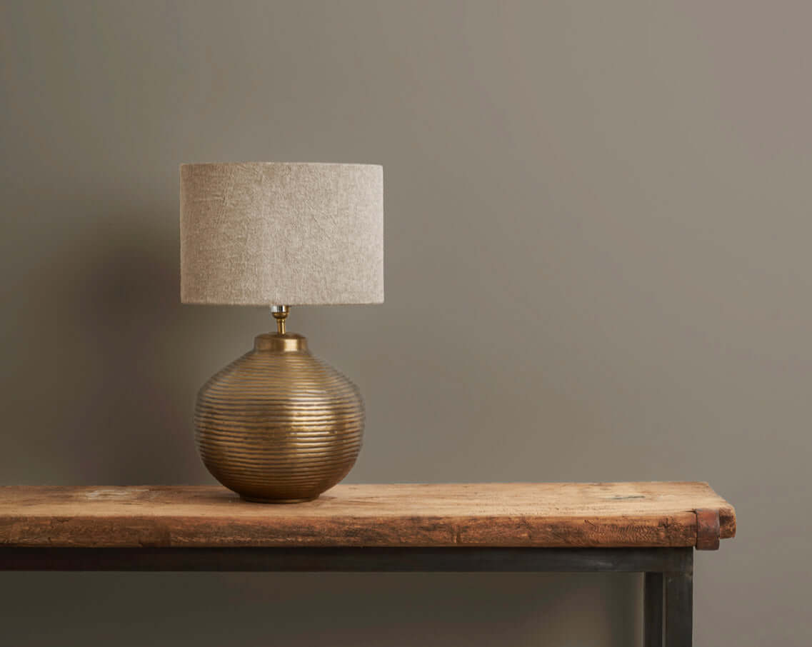 Stylish gold table lamp with textured shade on a rustic wooden table against a neutral wall.